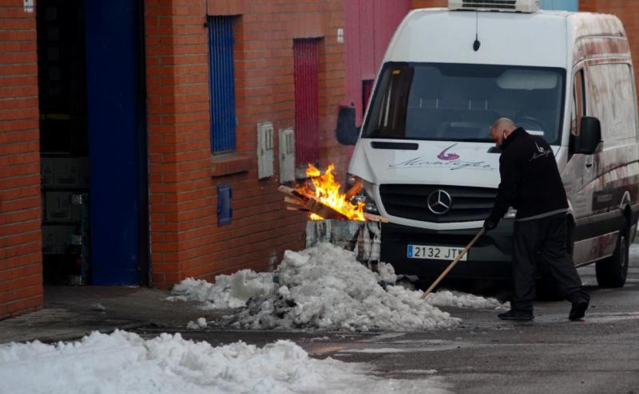 Una persona limpia la nieve helada delante de una nave con un bidón con fuego para calentar la zona.