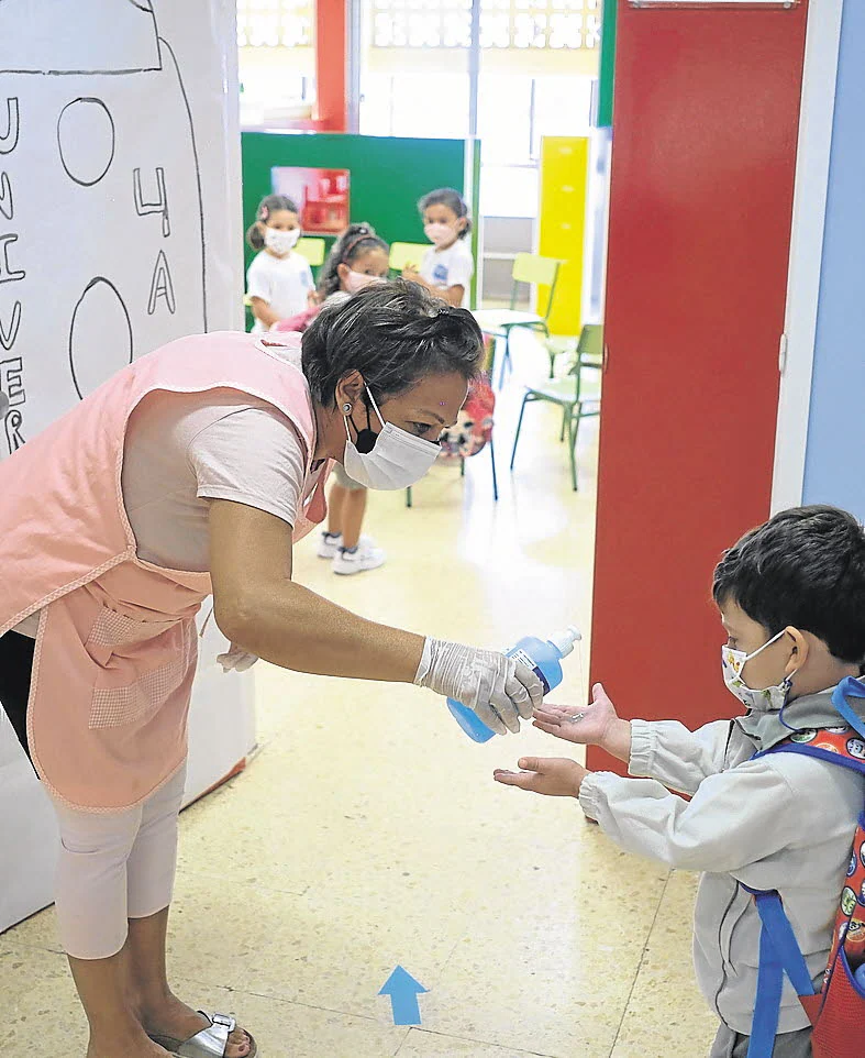 Una profesora pone gel desinfectante en las manos a un niño antes de entrar en la clase.