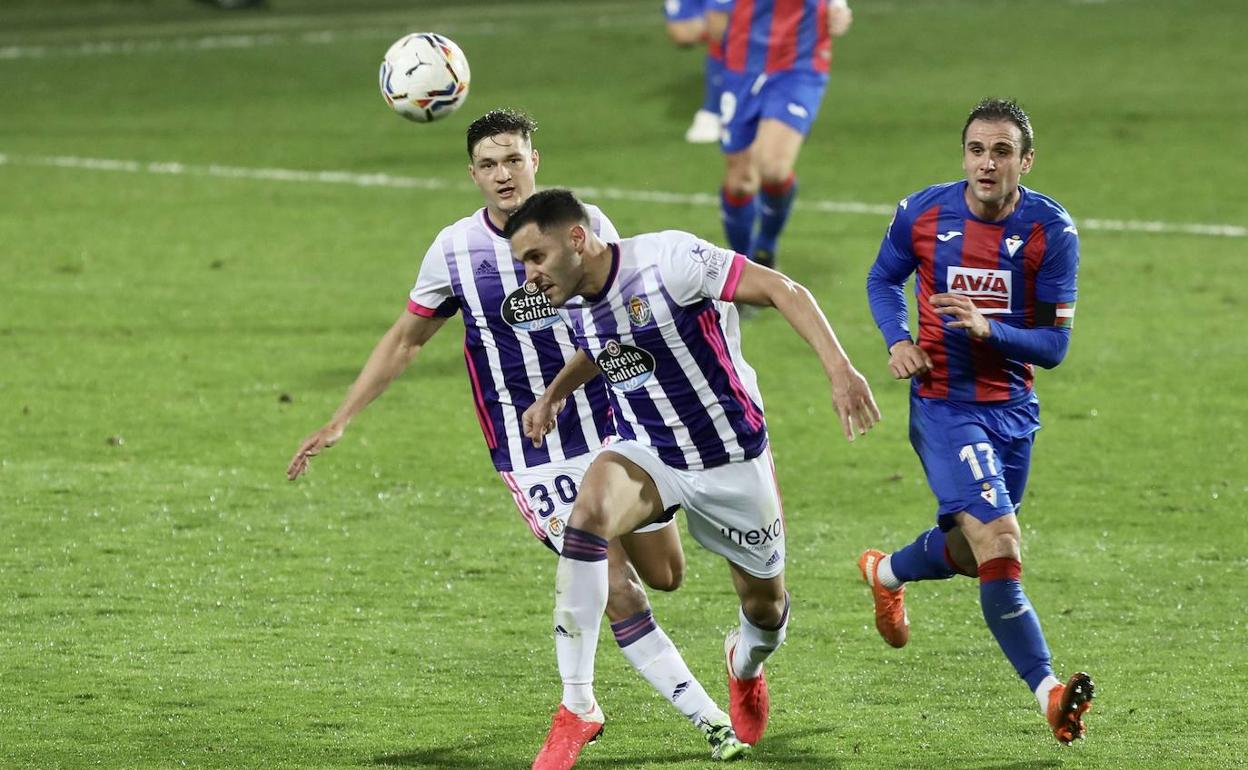 Bruno González despeja un balón ante su compañero Miguel Rubio y el delantero local Kike García durante el Eibar-Real Valladolid.