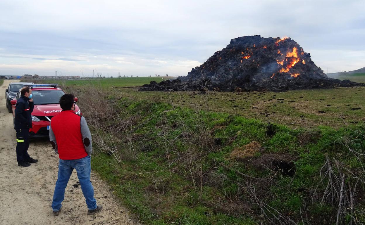 Javier, el propietario de los terrenos, conversa con un bombero ante la pila de pacas de paja ardiendo.