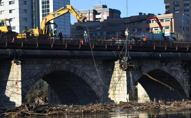 Tres máquinas sacan los troncos acumulados entre los pilares del Puente Mayor para ser troceados y trasladados a un solar de Girón.