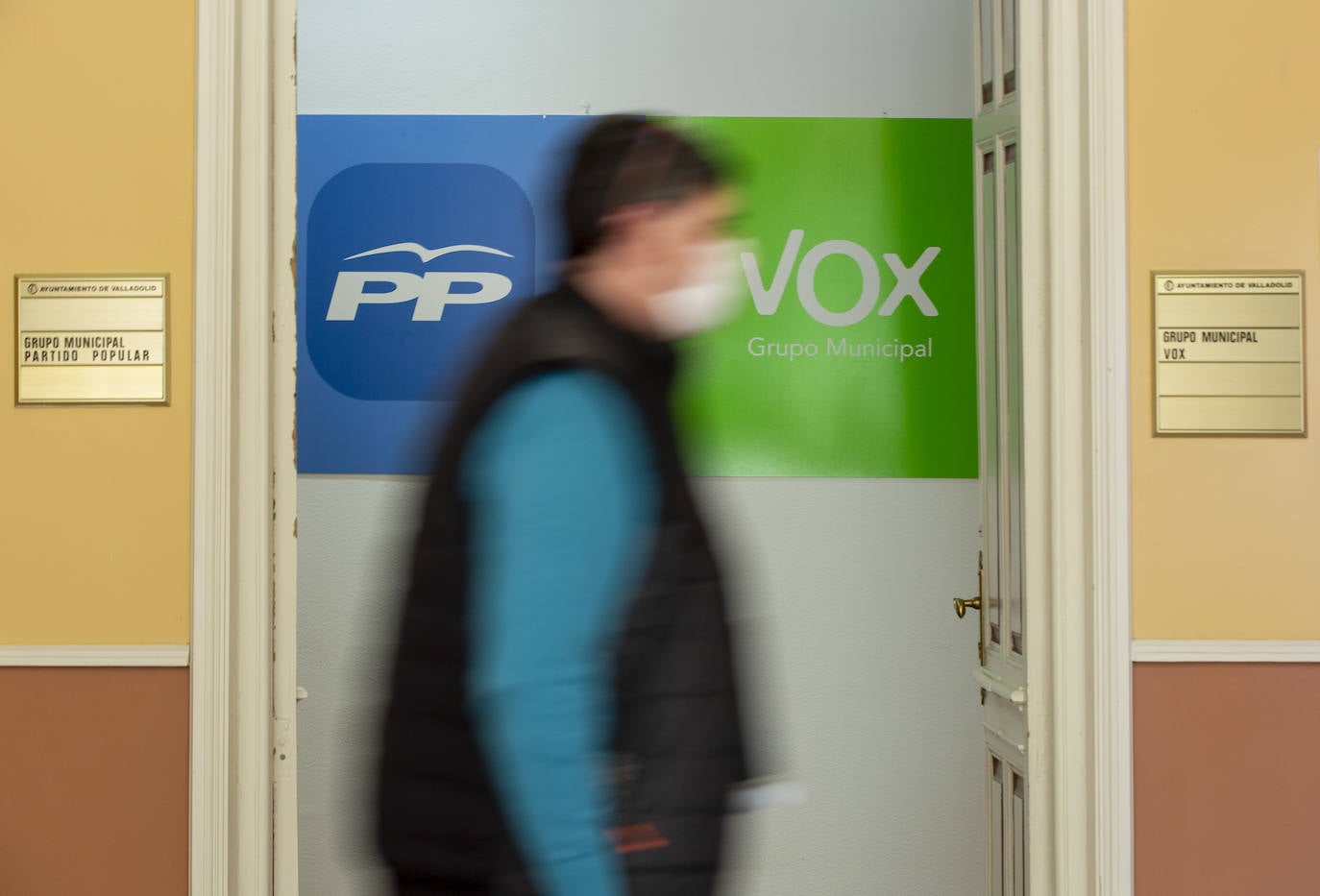 Un hombre pasa frente a las puertas de los grupos municipales de PP y Vox en el Ayuntamiento de Valladolid. 