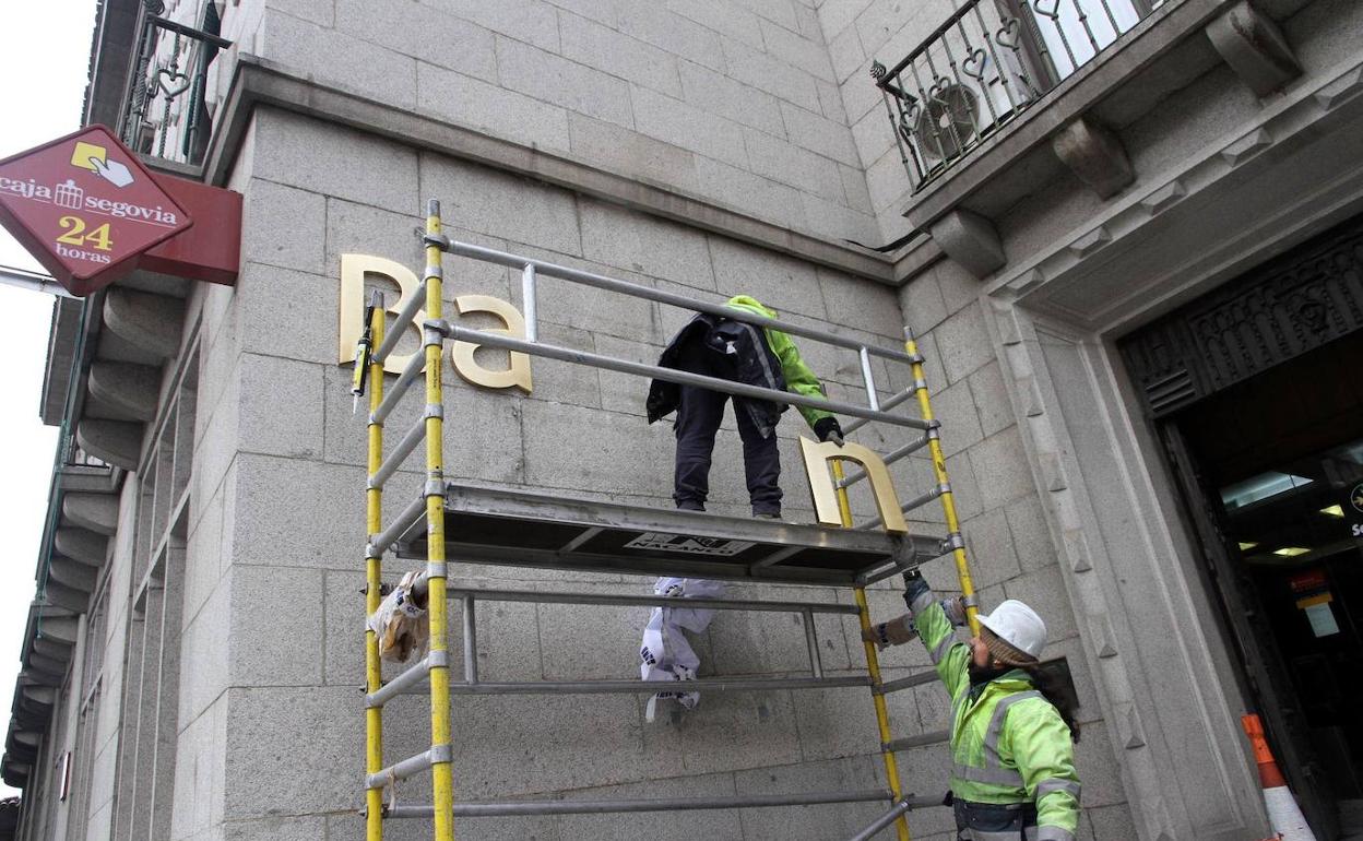 Operarios descuelgan las letras de 'Bankia' en la oficina principal para colocar el nuevo letrero de CaixaBank. 