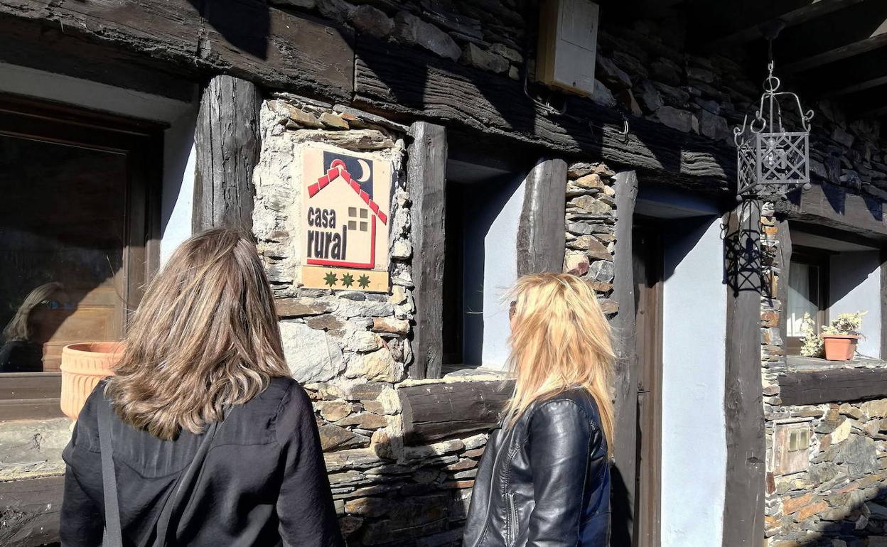 Dos mujeres miran el cartel de un alojamiento rural. 