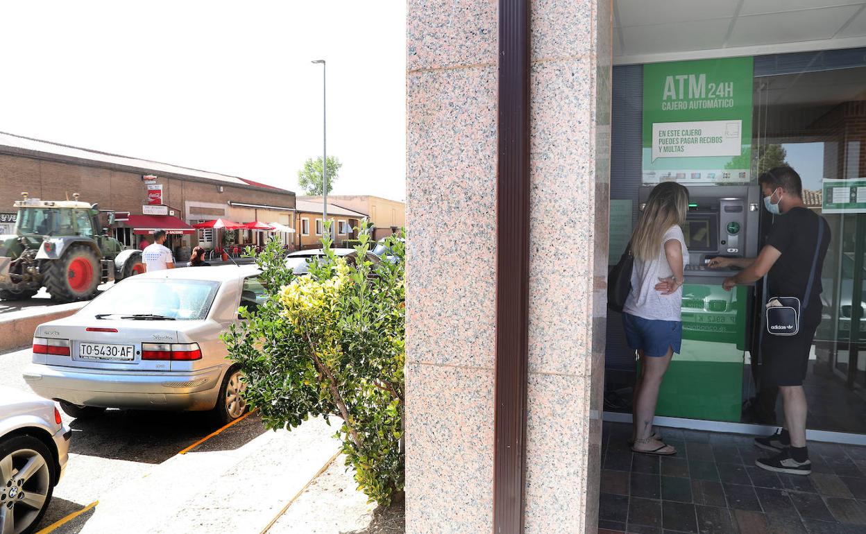 Dos jóvenes utilizan un cajero en una concurrida calle de Frómista. 