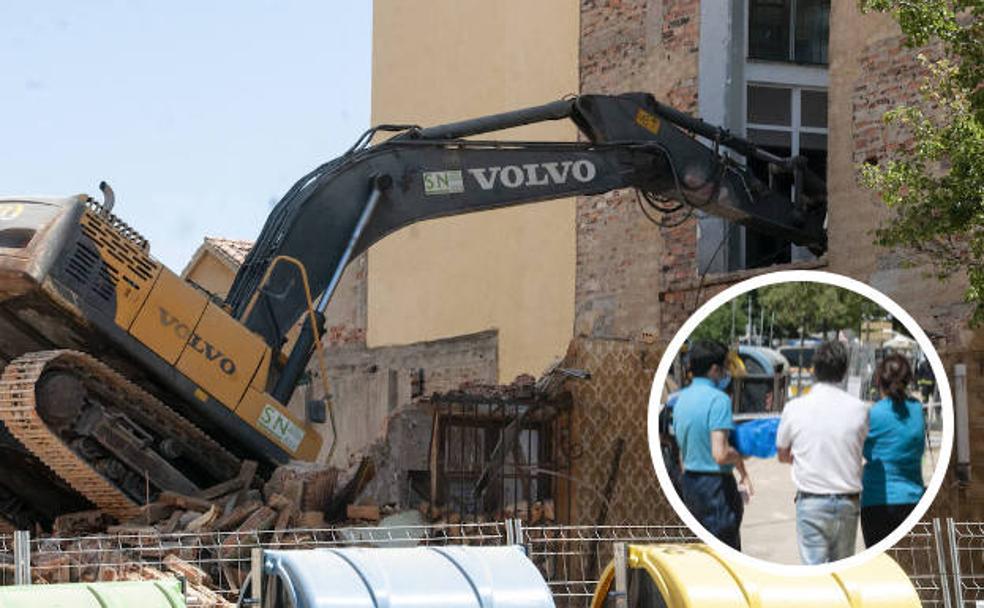 La pala de la oruga de demolición empotrada en el bloque de viviendas y en techo de un supermercado anexo. En el círculo, trabajadores de la tienda ven con tristeza los destrozos. 