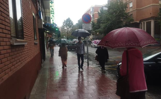 Varios vecinos de Valladolid se refugian de la lluvia con paraguas en la mañana de hoy martes.