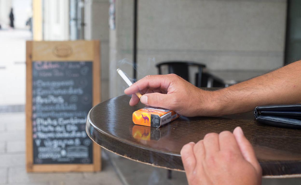 Un hombre fuma un cigarro en el velador de un establecimiento hostelero. 