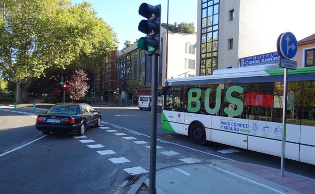 Imagen principal - Un coche y un autobús procedente de la vía de servicio, en el cruce del carril bici. Debajo, a la izquierda, el bolardo del carril bici. A la derecha, un usuario espera para cruzar. 