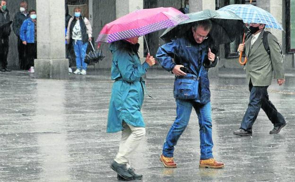 Tres personas se protegen de la lluvia con sus paraguas en la avenida del Acueducto. 