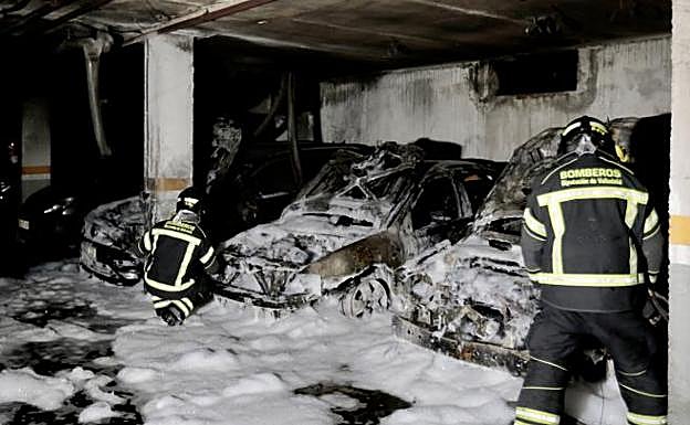 Dos bomberos examinan los tres coches incendiados, que rociaron con espuma, en el garaje comunitario del número 65A de la avenida de José Luis Lasa de Arroyo. 