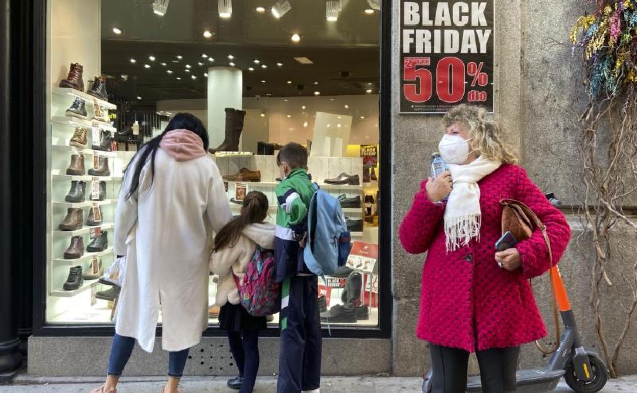 Varias personas en el escaparate de un comercio que anuncia descuentos del 50% por el Black Friday.