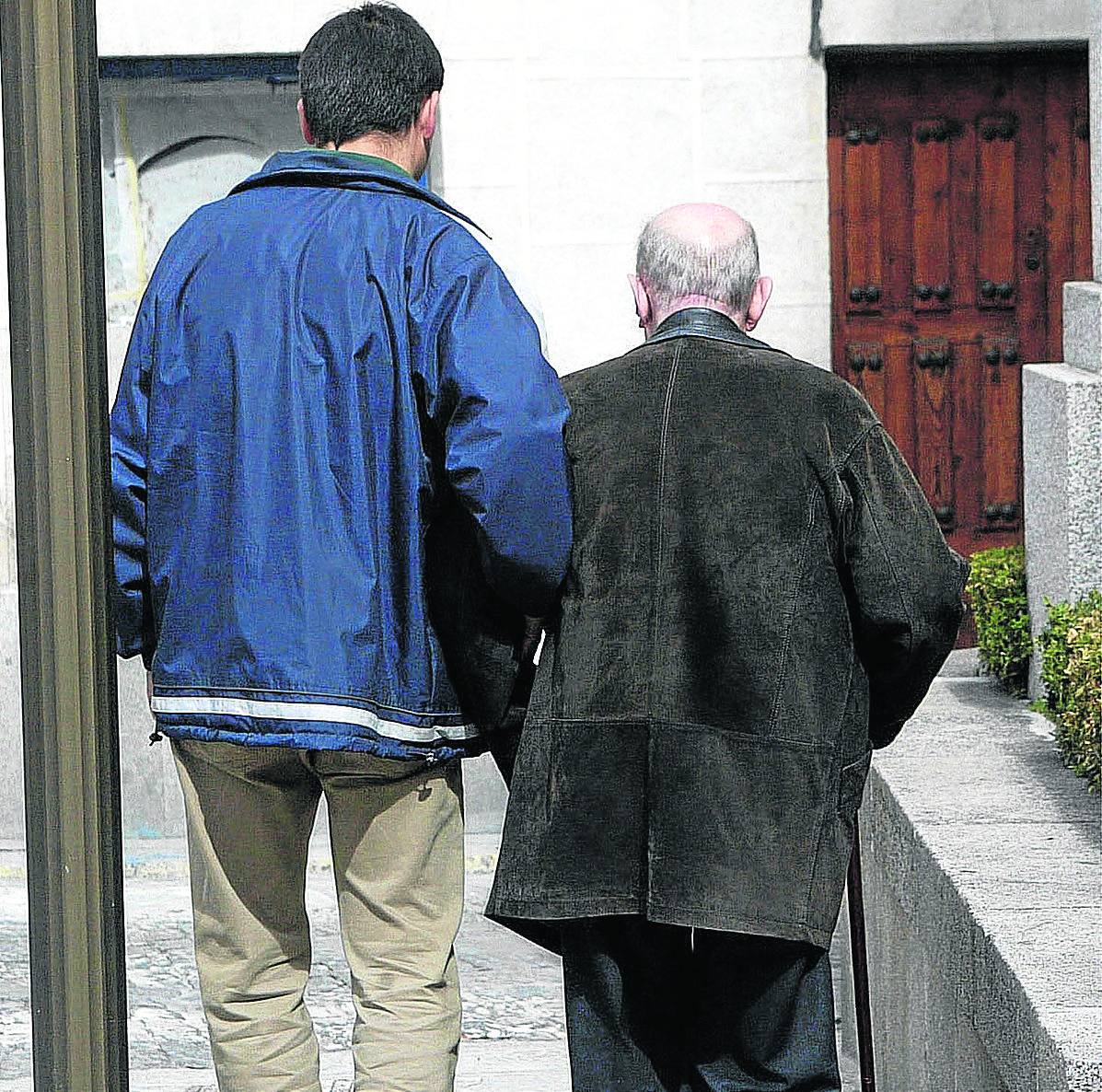 Un hombre ayuda en su paseo a un anciano por una calle de Segovia.