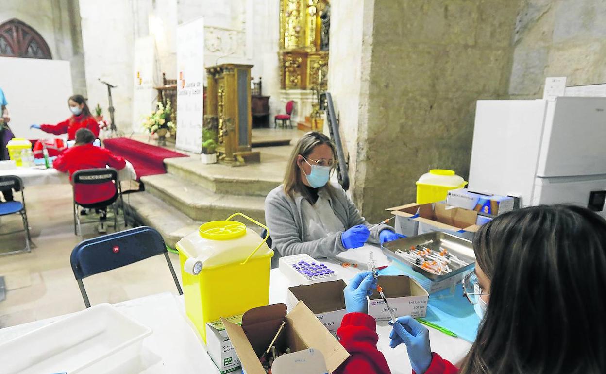 Dos profesionales del equipo de vacunación preparan las dosis en la iglesia de San Francisco, con una línea de vacunación al fondo.