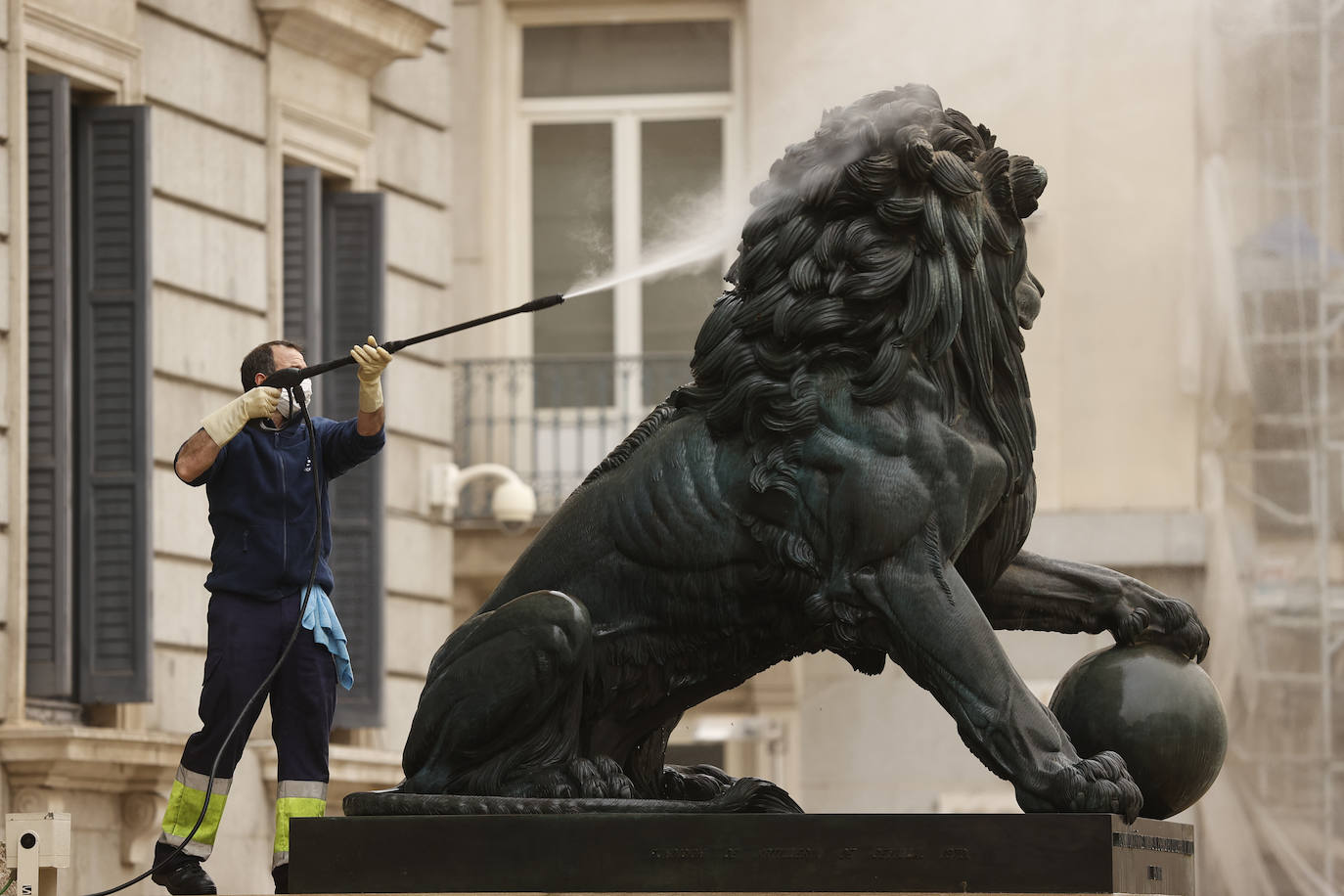 Un operario limpia uno de los leones que presiden el acceso al Congreso de los Diputados.