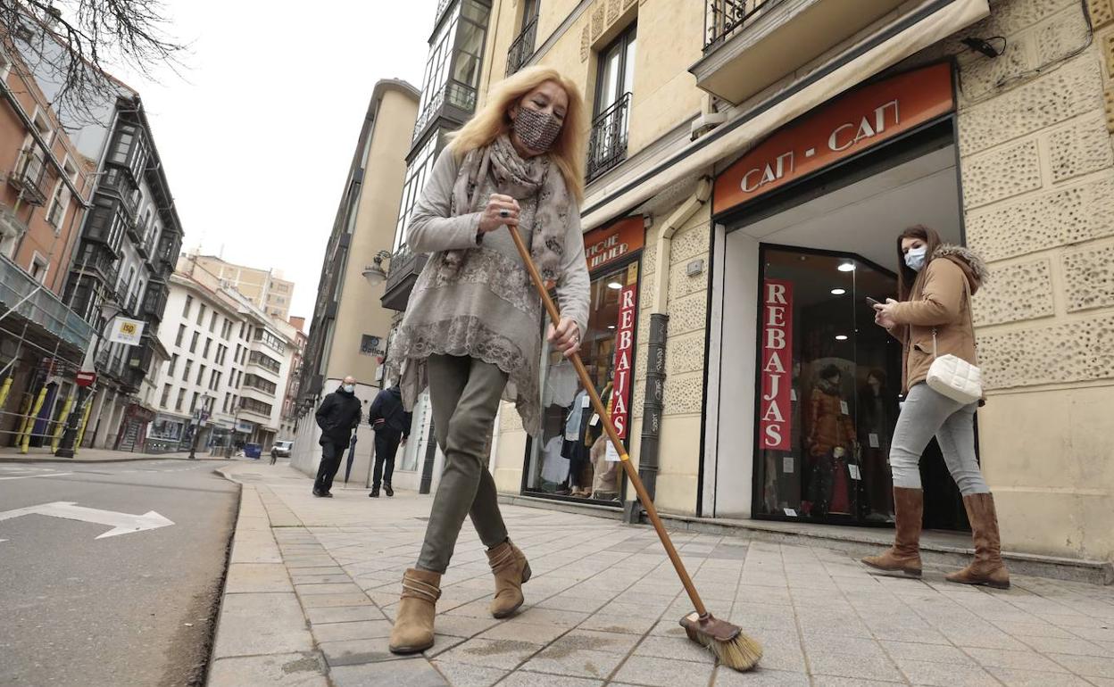 Una comerciante barre el polvo de la acera frente a su tienda en Valladolid. 