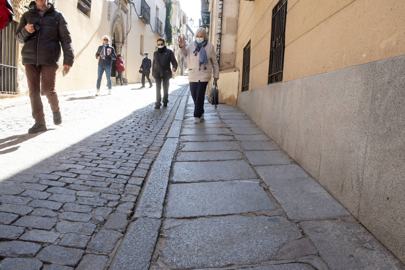 Peatones transitan por las maltrechas acera y calzada de Daoiz.