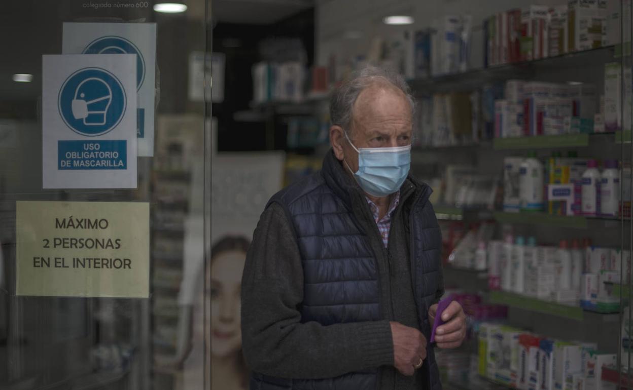 Una persona mayor sale de una farmacia con su mascarilla. 