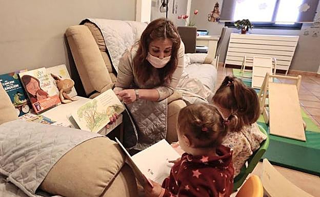 La educadora Noelia Rodríguez en el salón de su casa lee un cuento a las pequeñas Alba y Leia. 