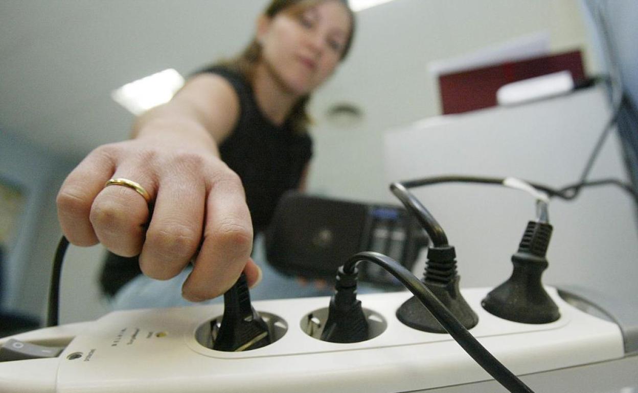 Una mujer enchufa un aparato en una regleta eléctrica.