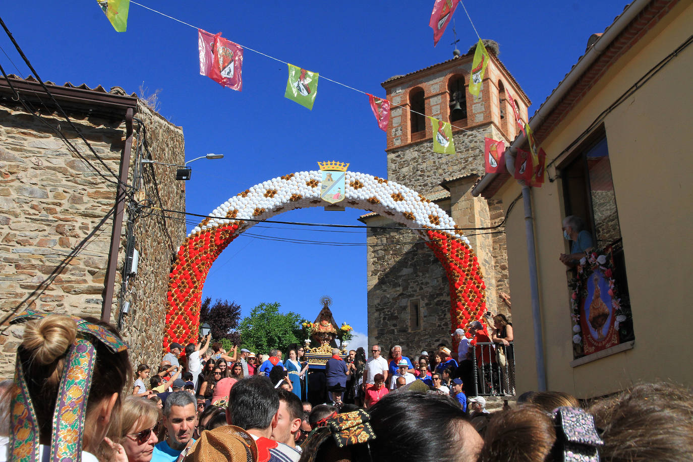 Los grupos de paloteo preceden el paso de la Virgen del Castillo por uno de los arcos de flores de papel en Bernardos. 