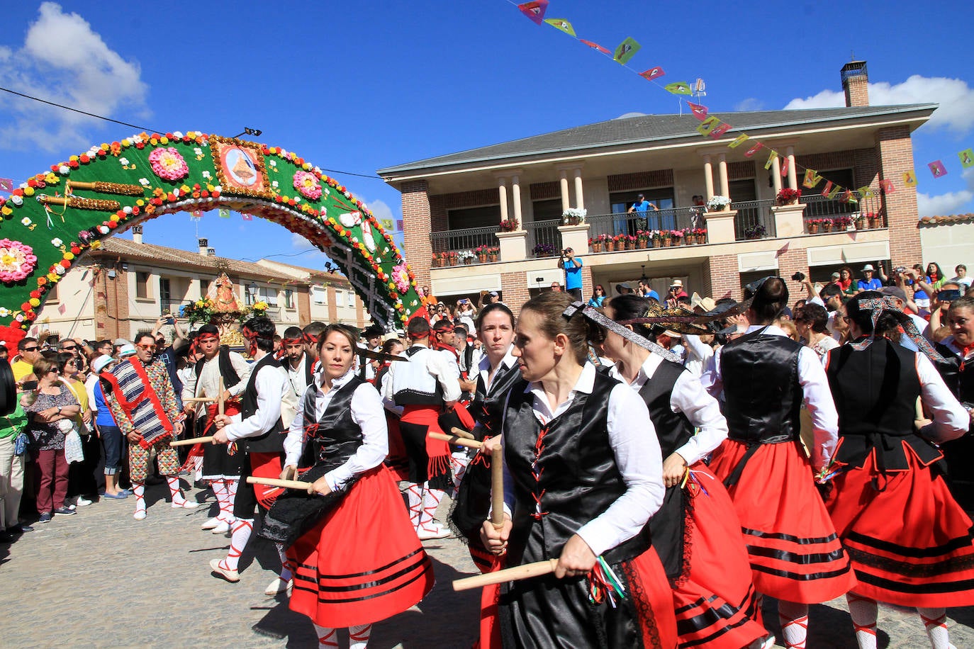 Los grupos de paloteo preceden el paso de la Virgen del Castillo por uno de los arcos de flores de papel en Bernardos. 