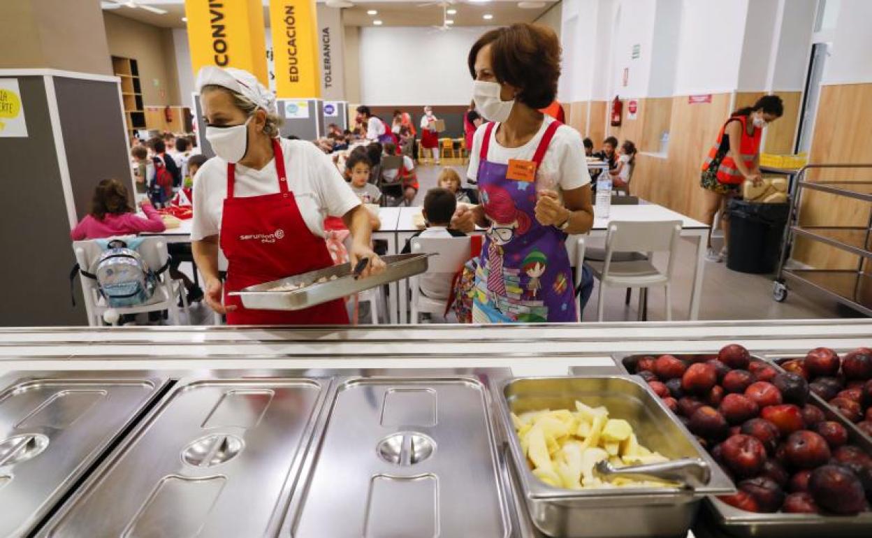 Varias trabajadoras sirven los platos a los niños en un comedor escolar. 