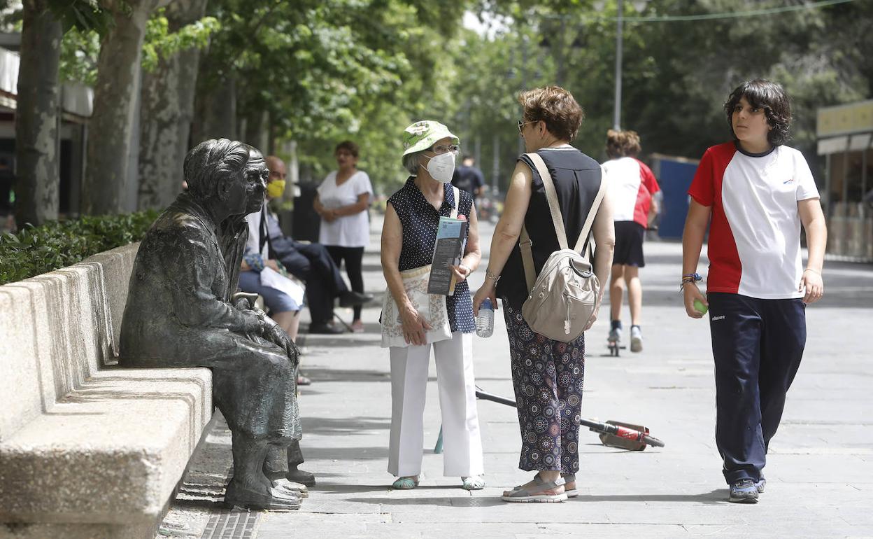 Dos mujeres conversan junto a la estatua a los mayores.