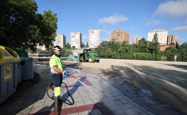 Un trabajador limpia la zona junto a la playa con una manguera. 