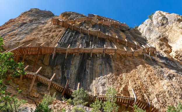 Montfalcó-Mont Rebei. (Huesca-Lleida). Viajamos a la muga de Huesca con Lleida para afrontar casi trescientos escalones anclados en gigantescas paredes de piedra. ¿Te atreves? El recorrido lineal de unos 8 kilómetros se divide en dos partes, la zona oscense y la leridana. Comienza en Huesca en el refugio de Montflacó, al este del embalse de Canelles, y en una hora escasa aparece el primer tramo de escaleras para salvar en zig-zag 33 metros de altura. Tras superarlo, el camino nos da un respiro de unos 20 minutos.