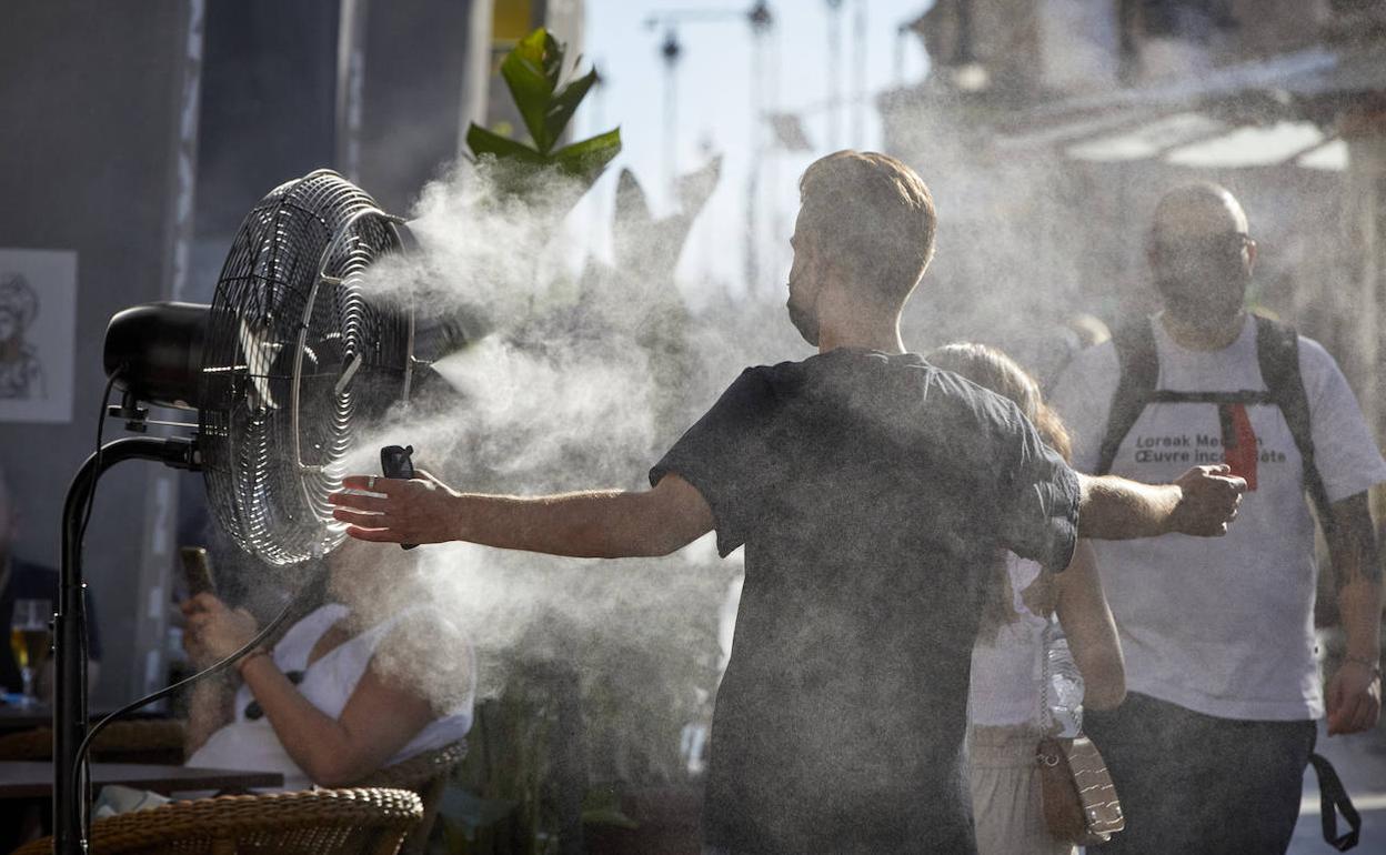 Un joven se refresca con un difusor de vapor de agua instalado en la terraza de un restaurante.