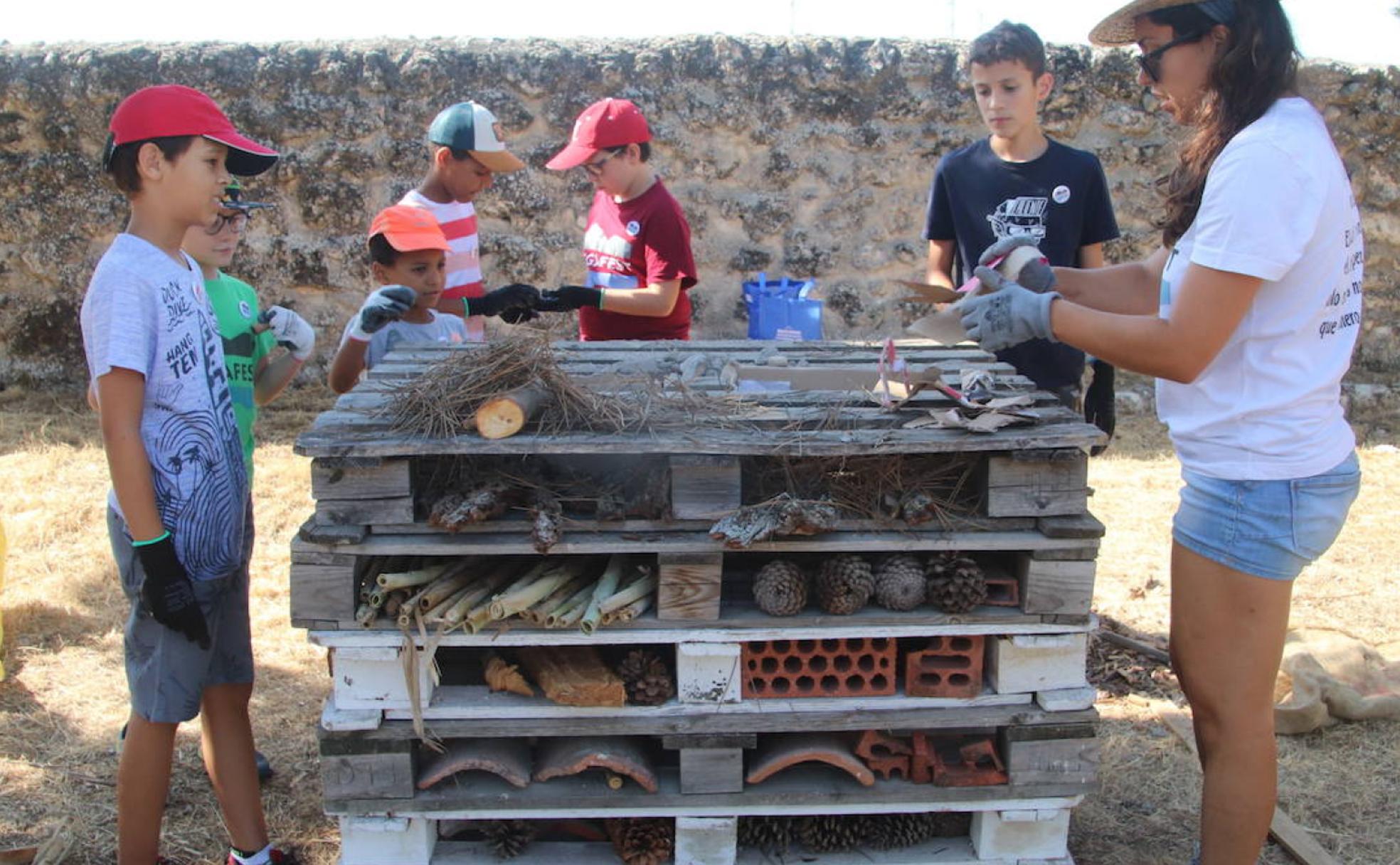 La monitora guía a los niños en la elaboración de los diferentes 'hogares' para insectos sobre unos palés. 