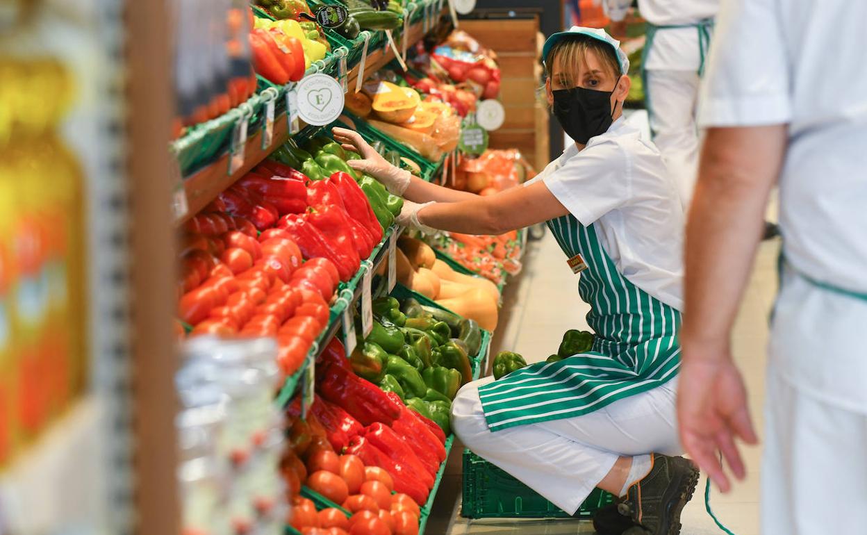 Una trabajadora de un supermercado coloca la sección de frutas y verduras.