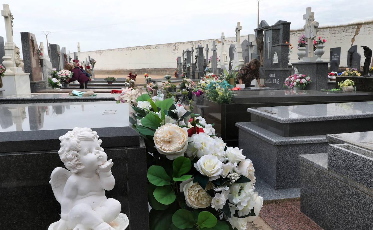 Dos mujeres limpian sepulturas, estos días previos a Todos los Santos.