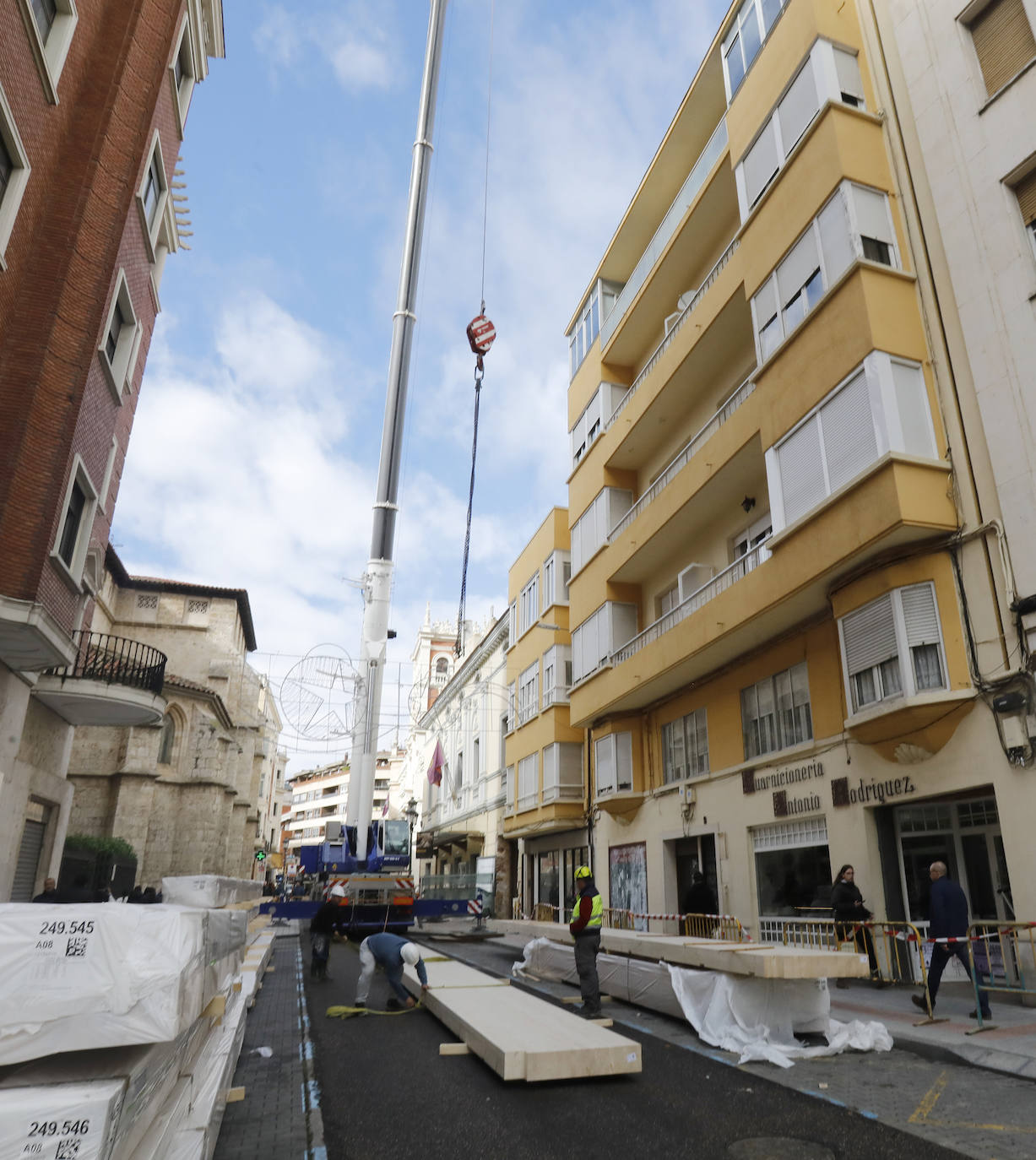 Una grúa de grandes dimensiones trabaja en la calle Burgos para colocar decenas de vigas de madera de tamaño gigante.