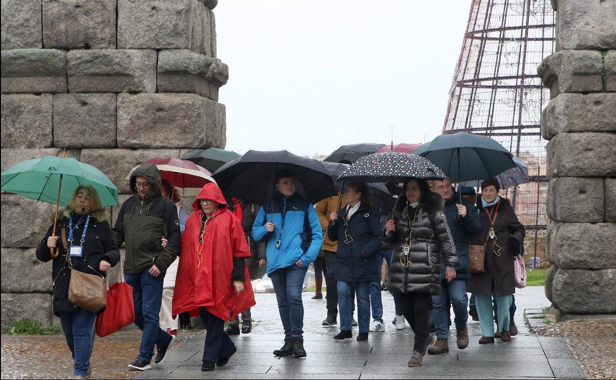 Un grupo de turistas, con chubasqueros y paraguas, en el Azoguejo.