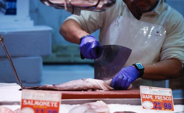 Un pescatero prepara un pescado en un puesto de un mercado. 