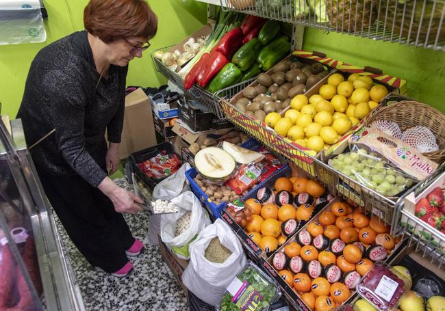 Una comerciante coge legumbres en su tienda de alimentación.