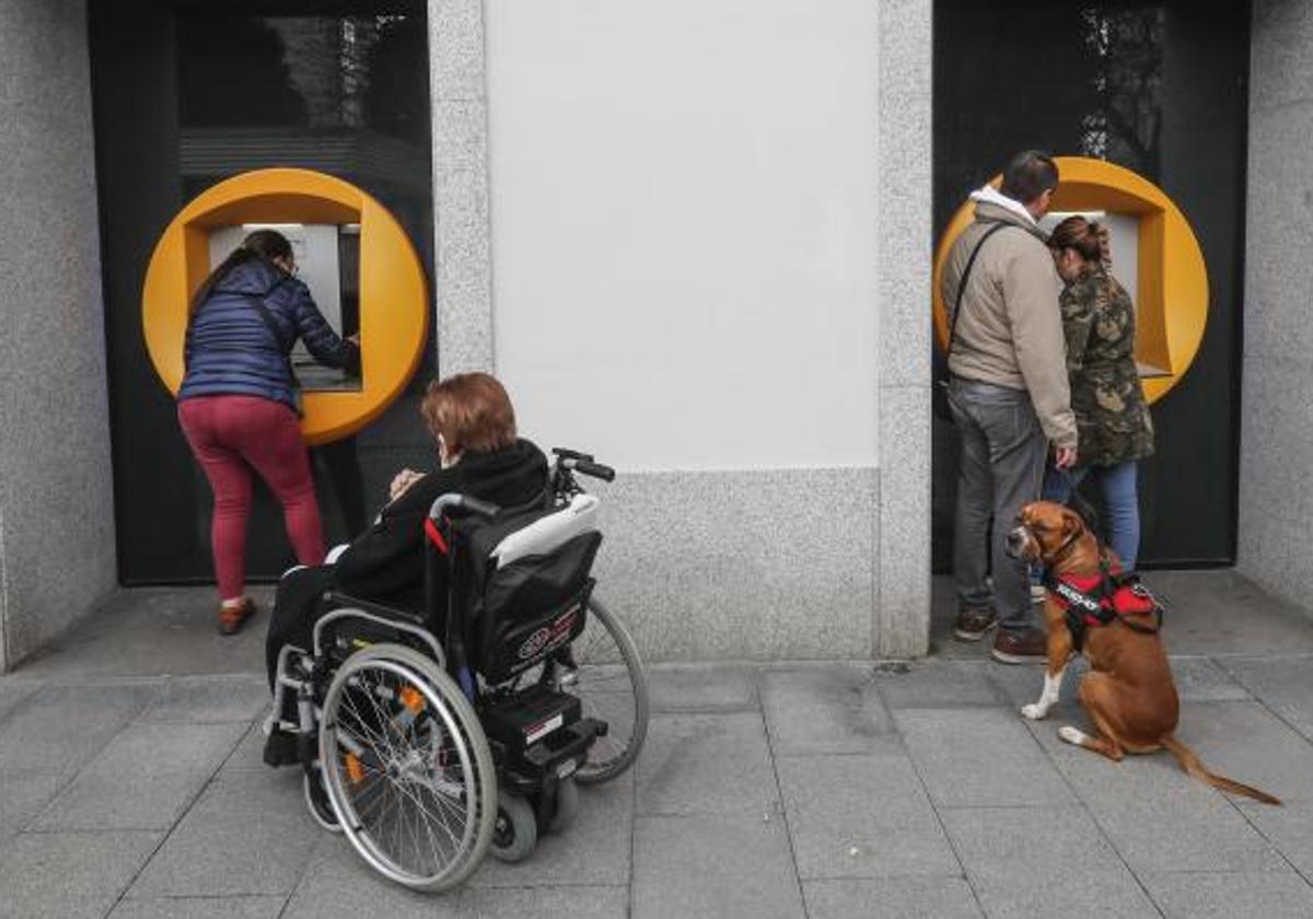 Varias personas sacan dinero de los cajeros automáticos de una entidad financiera.