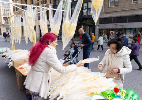 Imagen secundaria 1 - Arriba, Diana Mongil en su puesto de la Plaza España. A la izquierda, Rosa María A. García vende una palma a una abuela. A la derecha, Javier y su hijo Adrián tras comprar una palma en la calle Santiago.