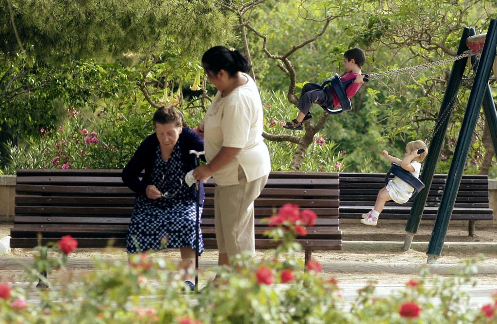 Una cuidadora extranjera atiende a una anciana en un parque.