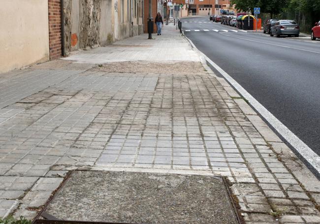 Acera con baches y baldosas rotas en la carretera de Villacastín, recién asfaltada.