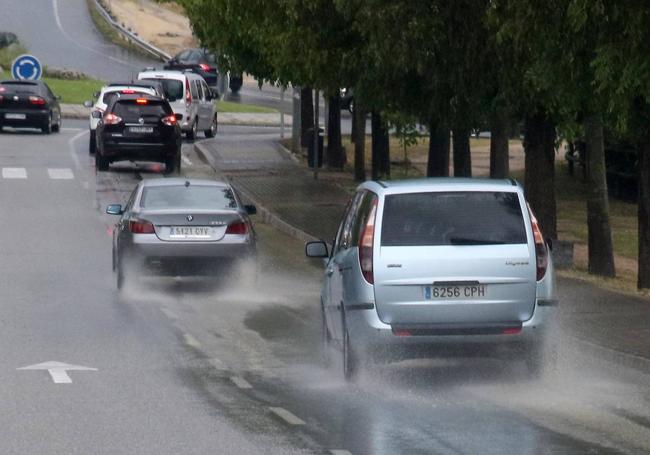 Tráfico de vehículos este martes por la tarde bajo la lluvia y surcando algunos charcos en las calzadas.