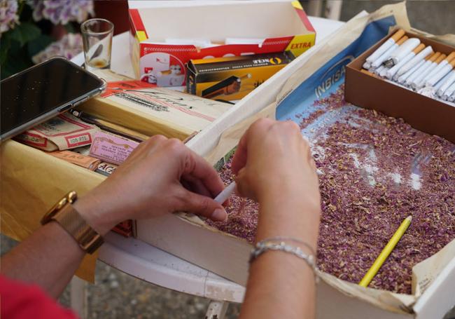 Una vecina rellena un tubo de cigarrillo con la picada de pétalos de rosas