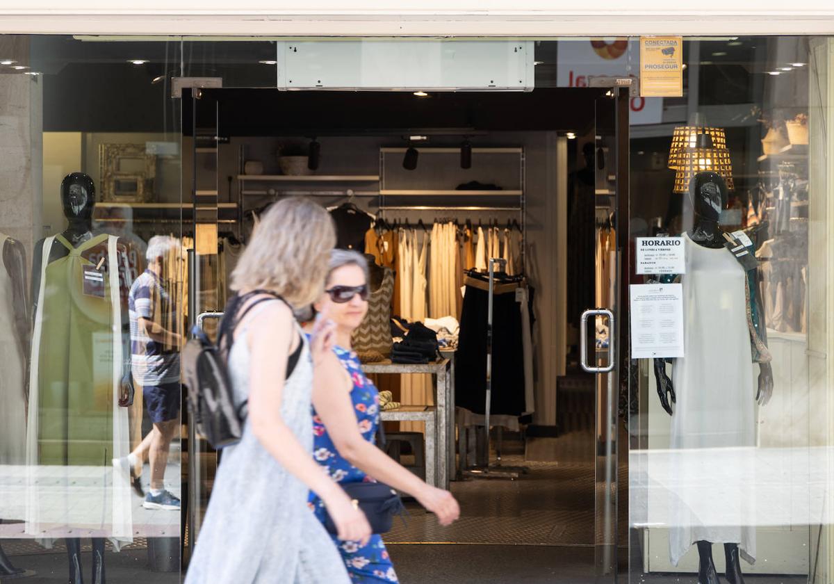 Dos mujeres caminan por delante de un comercio, con la puerta abierta de par en par.