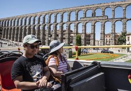 Un par de turistas extranjeros viajan en la parte de arriba del autobús turístico, este martes, en Segovia, con el Acueducto al fondo.
