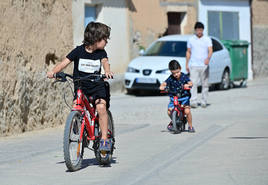 Tony y Alfonso juegan con sus bicis, bajo la mirada de su padre, en la calle de Valbuena en la que viven.