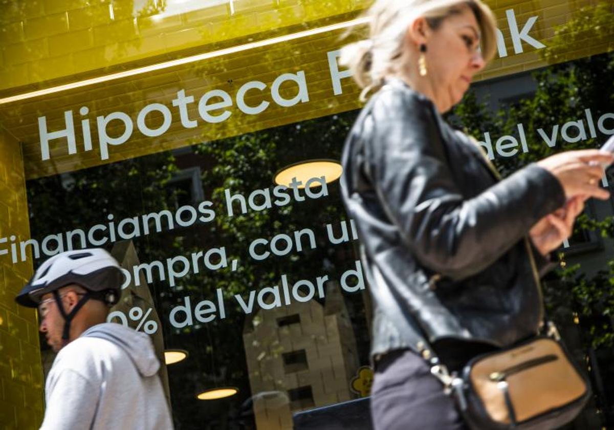 Viandantes junto a un anuncio bancario de préstamos hipotecarios.