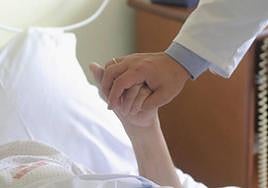 Un sanitario sostiene la mano de una enferma terminal.