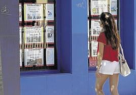 Una joven mira un escaparte con anuncios de pisos en alquiler.